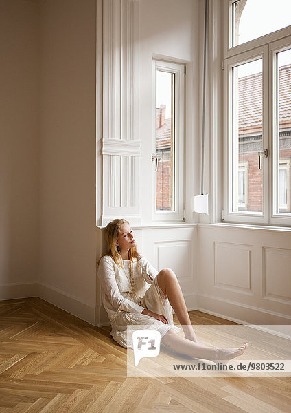 Junge blonde Frau sitzt in Wohnung auf dem Boden