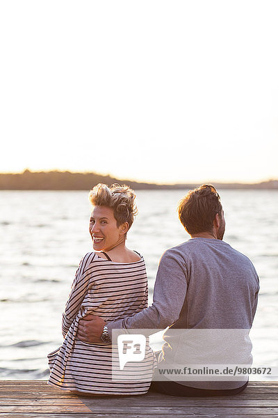 Rückansicht Porträt einer glücklichen Frau  die mit einem Mann am Pier gegen das Meer sitzt.