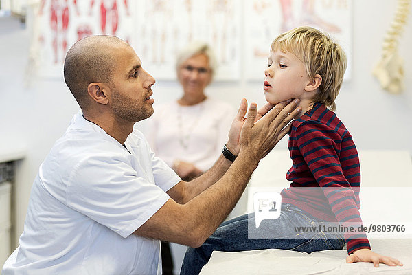 Seitenansicht des männlichen Arztes  der den Hals des Jungen in der Klinik untersucht.