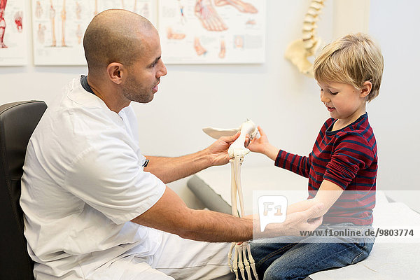 Männlicher Arzt erklärt dem Jungen in der orthopädischen Klinik das Handmodell