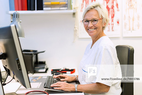 Porträt eines glücklichen leitenden orthopädischen Chirurgen mit Computer am Schreibtisch in der Klinik