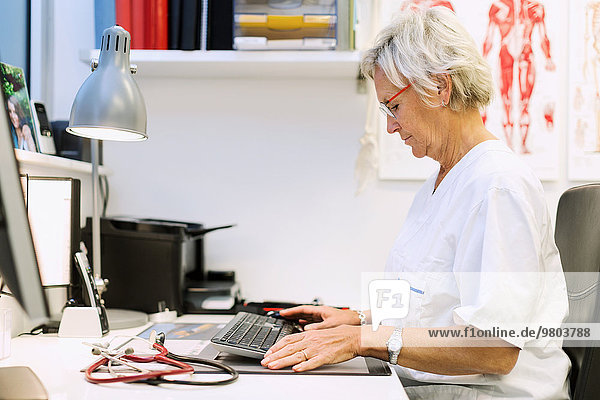 Seitenansicht des leitenden orthopädischen Chirurgen mit Computer am Schreibtisch in der Klinik