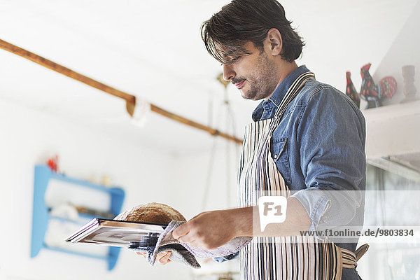 Side view of man holding freshly baked bread in tray at home