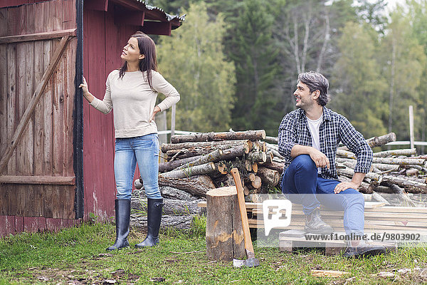 Man looking at woman holding open barn door while sitting by firewood