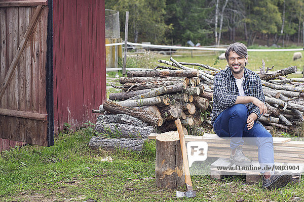 Portrait of man sitting on wooden planks against stacked firewood at yard