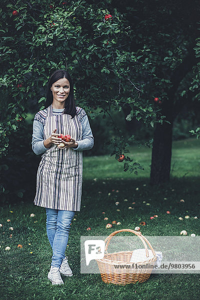 Porträt einer lächelnden Frau mit frischen Äpfeln im Obstgarten.