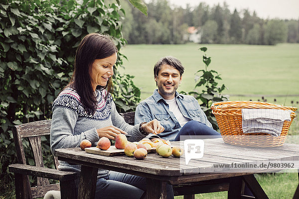 Happy man looking at woman cutting apples at table in organic farm
