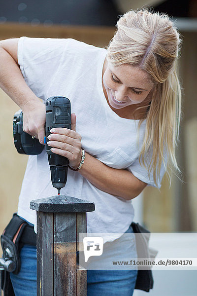 Happy woman using cordless screwdriver on wooden post