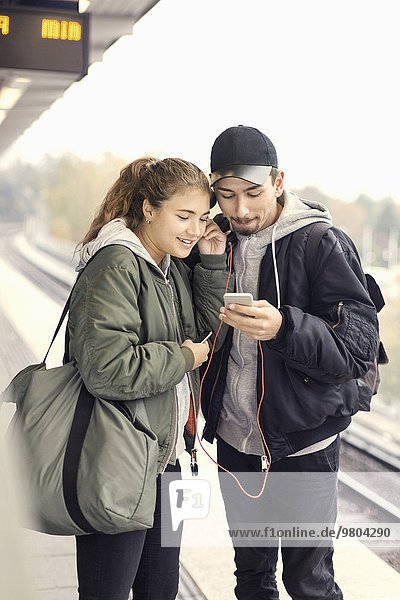 Young couple listening music through mobile phone on subway platform