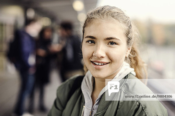 Porträt eines lächelnden Studenten an der U-Bahn-Station mit Freunden im Hintergrund