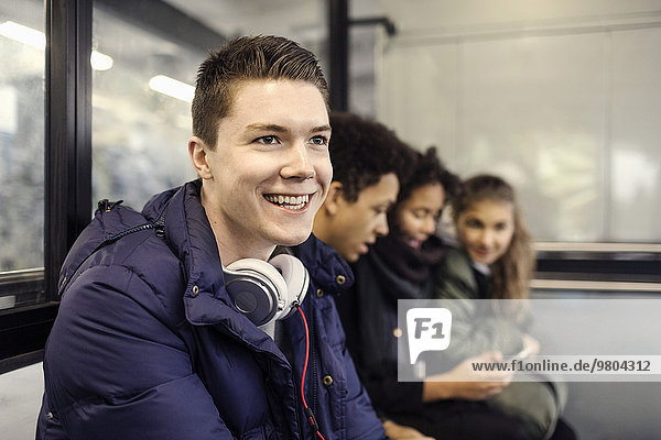 Happy male university student sitting with friends at subway station