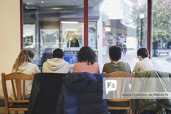 Rückansicht von multiethnischen Freunden  die auf Stühlen in der Cafeteria sitzen.