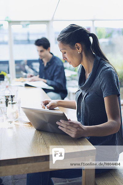 Frau mit digitalem Tablett mit männlichem Freund im Hintergrund im Cafe