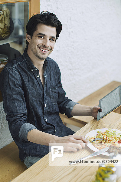 Porträt eines glücklichen Mannes mit digitalem Tablett beim Mittagessen im Cafe
