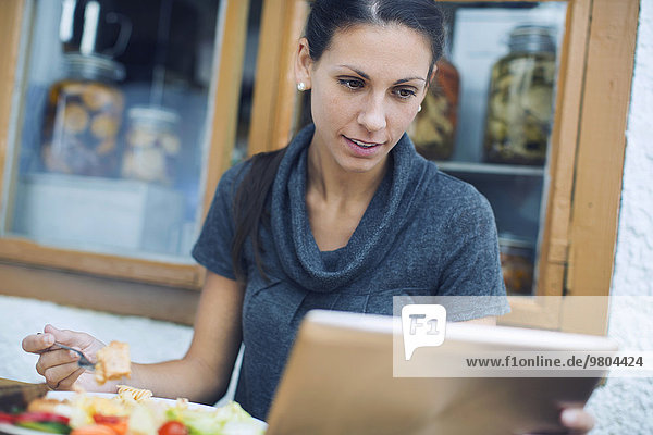 Frau mit digitalem Tablett beim Mittagessen im Cafe