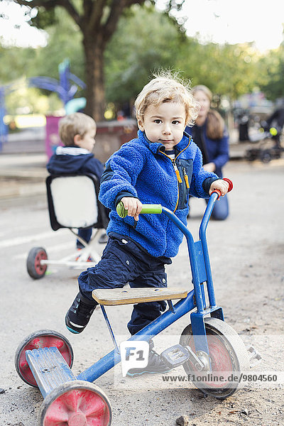 Porträt eines Jungen  der mit einem Dreirad auf dem Spielplatz spielt.
