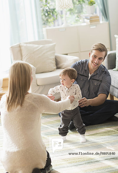 Happy parents helping little son (2-3 years) walking in living room