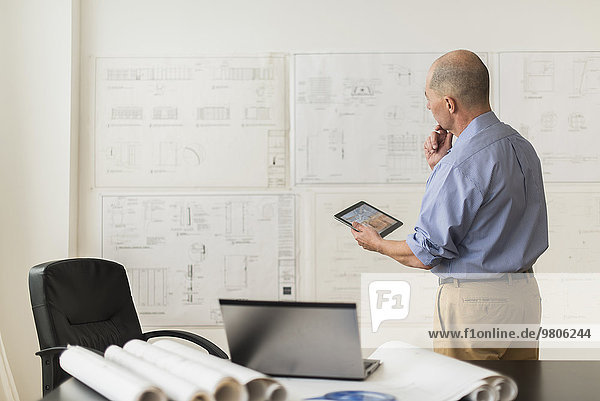 Mature architect looking at blueprints in office