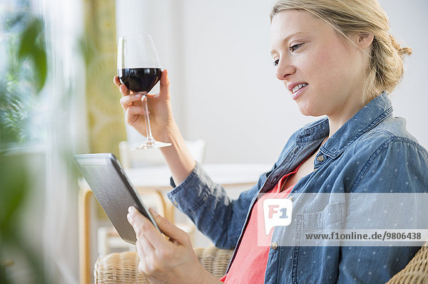 Woman sitting with digital tablet and glass of red wine