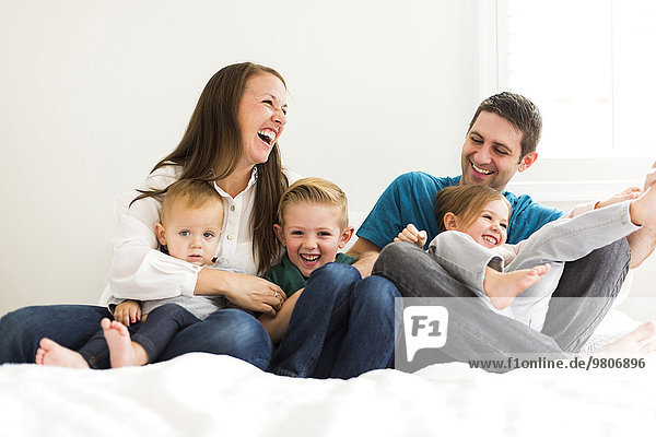 Family with three children (2-3  4-5) laughing on bed