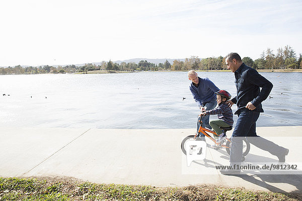 Männliches Paar läuft neben dem Sohn auf dem Fahrrad im Park