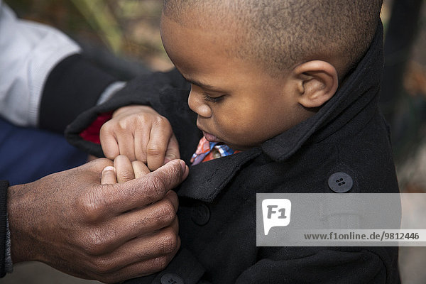 Close up of male toddler buttoning jacket in park