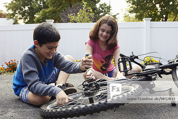 Bruder und Schwester reparieren Fahrrad auf der Einfahrt