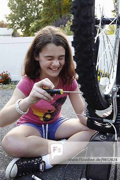Lachendes Mädchen repariert Fahrrad auf der Einfahrt