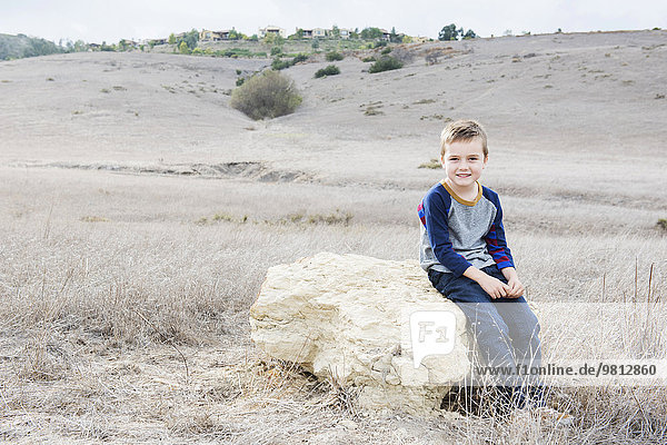 Porträt eines Jungen auf einem Felsen sitzend