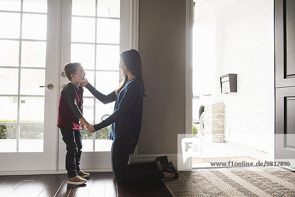 Mother kneeling and holding hands with son in living room
