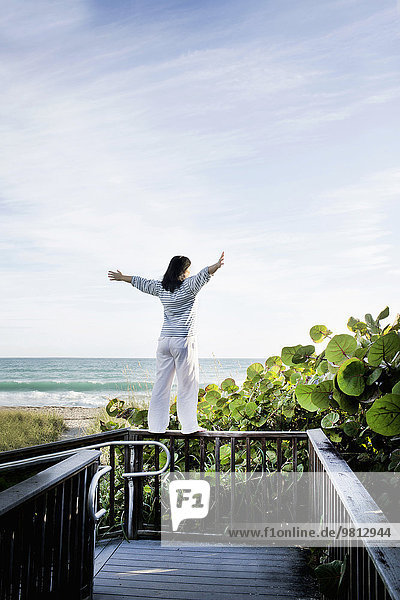 Mature woman with arms open on top of walkway railing  Juno Beach  Florida  USA
