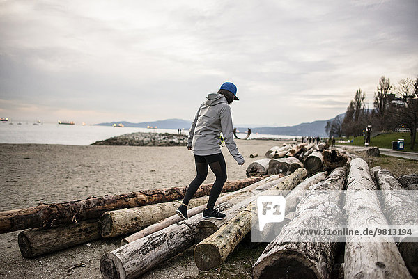 Junge Frau auf Baumstämmen  Rückansicht  Englische Bucht  Vancouver  Kanada