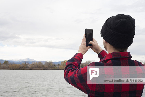 Mid adult man holding smart phone  taking photograph of view  rear view