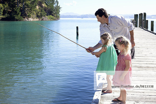 Mature man and two young girls fishing from pier  New Zealand