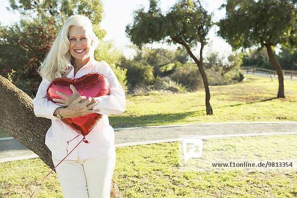 Senior Frau umarmt roten herzförmigen Ballon  Hahn Park  Los Angeles  Kalifornien  USA