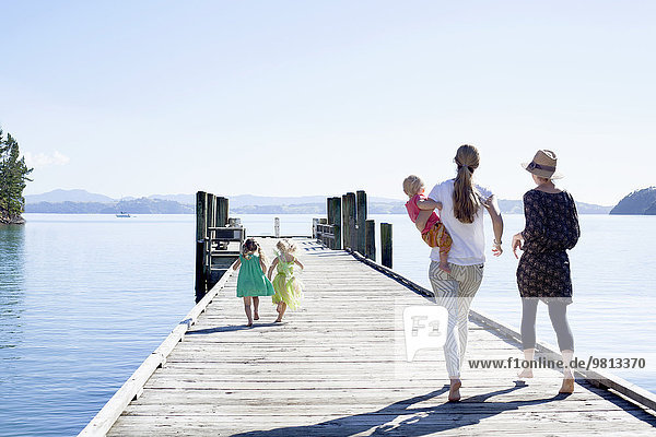 Two mid adult women and daughters strolling on pier  New Zealand
