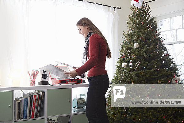 Junge Frau  die zu Weihnachten Vinyl auf Plattenspieler legt