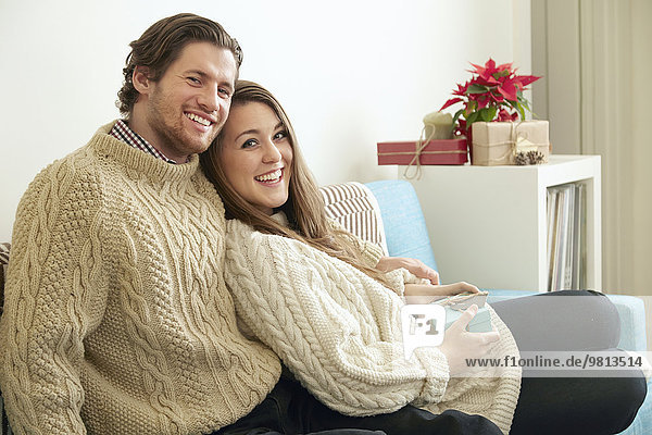 Portrait eines jungen Paares auf Sofa mit Weihnachtsgeschenk
