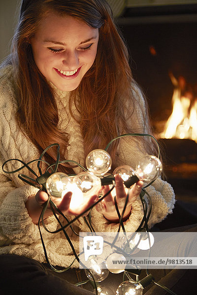 Young woman in living room holding illuminated christmas lights