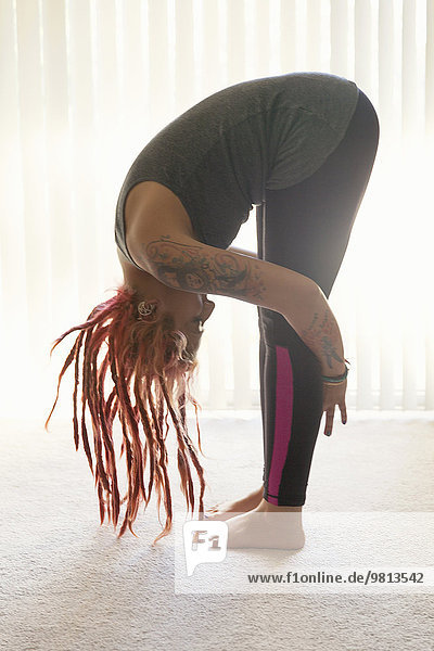 Young woman with pink dreadlocks practicing yoga in living room