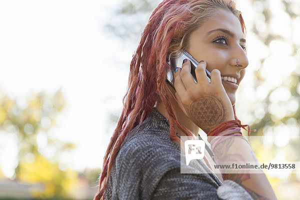 Young woman with pink dreadlocks chatting on smartphone in park