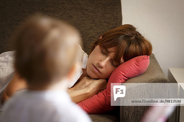 Mittlere erwachsene Frau  die auf dem Wohnzimmersofa schläft und von ihrer Tochter beobachtet wird.
