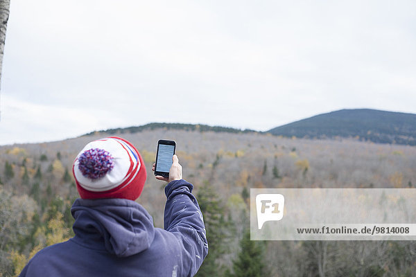 Rückansicht eines männlichen Wanderers beim Lesen von Smartphone-Texten in Landschaft  Rangeley  Maine  USA