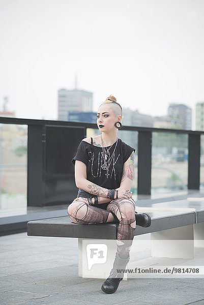 Portrait of young female tattooed punk sitting rooftop wall