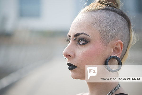 Porträt einer jungen Punkerin mit Ohrläppchenpiercing und rasiertem Kopf