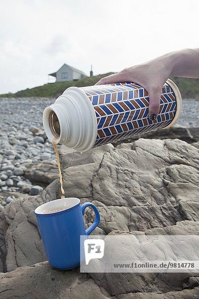 Weibliche Hand gießt Tee aus Getränkeflaschen am Millook Beach  Cornwall  UK