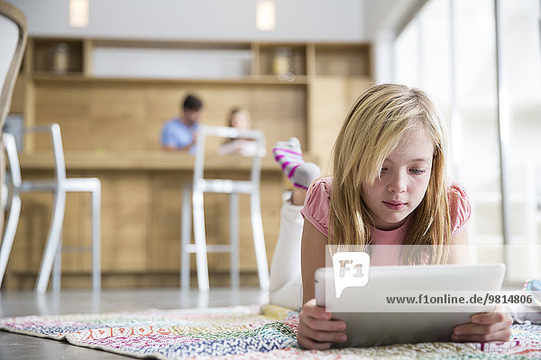Mädchen auf einem Teppich liegend  mit digitalem Tablett im Wohnzimmer