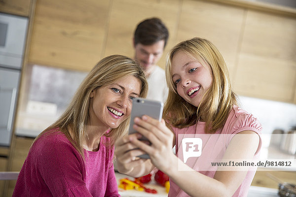 Mittlere erwachsene Frau und Tochter nehmen Smartphone Selfie im Esszimmer