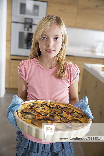 Portrait of girl carrying homemade aubergine  spinach and onion quiche in kitchen