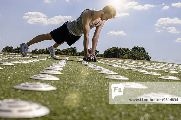 Young man doing push ups with hand weights on sports field